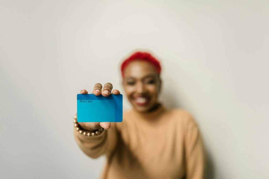 SV Luxe Resort Membership Programme A cheerful woman with red hair displays a blue card against a neutral background, focused on the card.