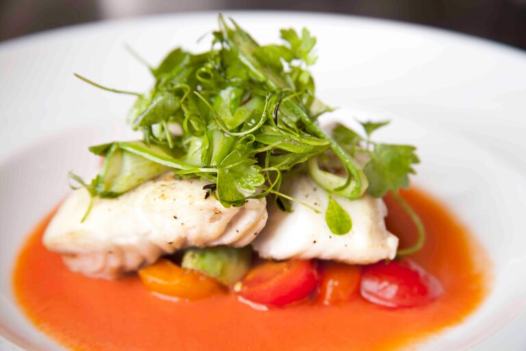 A beautifully presented gourmet fish dish topped with fresh herbs and vibrant vegetables.